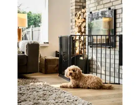 Kutyarács a Baby Dantól. A Dog Space MAX L kutyarács látható a képen. A kutyarács fekete színű. Összeszerelt állapotban van a kutya rács. Egy kutya fekszik előtte, mely megvédő a kandalló veszélyeitől.